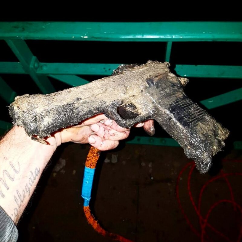 Vondstfoto van een roestig, met modder bedekt pistool dat met een vismagneet uit het water is gehaald tijdens magneetvissen.