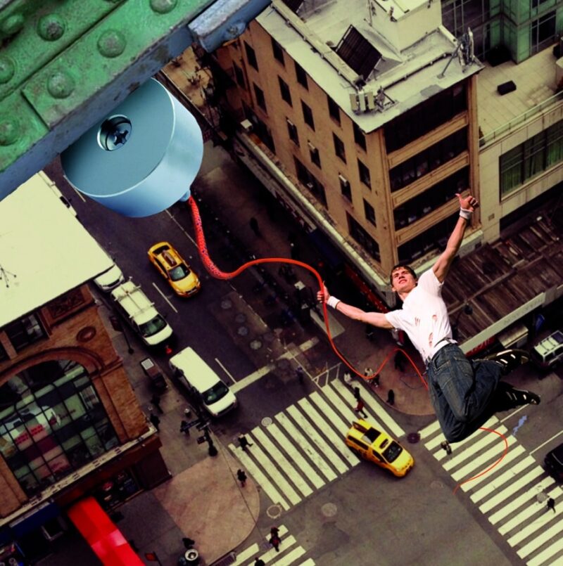 Creatieve bewerkte afbeelding van een man die bungelt aan een dik touw bevestigd aan een grote vismagneet boven een stad.