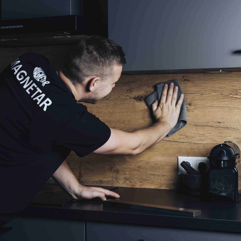 Man maakt houten keukenwand schoon met doek ter voorbereiding op het plaatsen van een magnetische messenstrip.