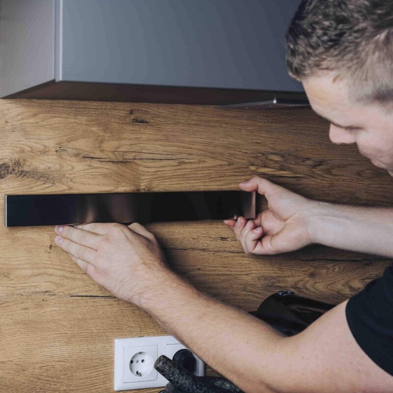 Man monteert een magnetische messenstrip op een houten keukenwand voor veilige en ruimtebesparende messenopslag.