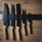 Magnetische messenstrip met zwart metalen messen en houten handvatten, stijlvol opgehangen aan houten keukenwand.