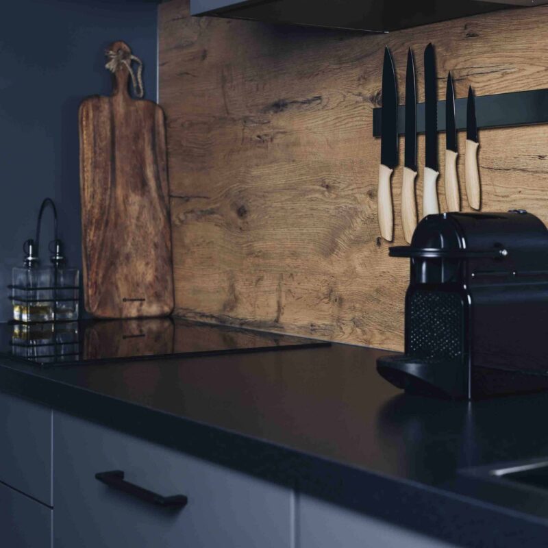 Moderne keuken met houten achterwand, magnetische messenstrip met zwarte messen en houten handvatten naast een koffiemachine.