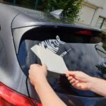 Witte Magnetar sticker wordt aangebracht op achterruit van auto, ideaal als merchandise voor magneetvissers.