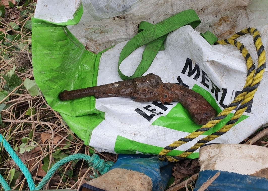 Magneetvissen vondst van een oud en roestige pistool, ook is er een plastic tas en een zwart/geel touw te zien