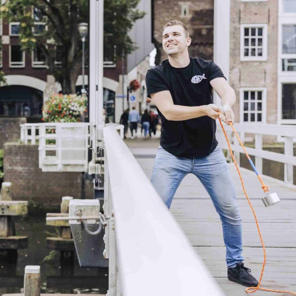 Een man met een zwarte Magnetar shirt gooit een sterke magneet voor magneetvissen vanaf een brug