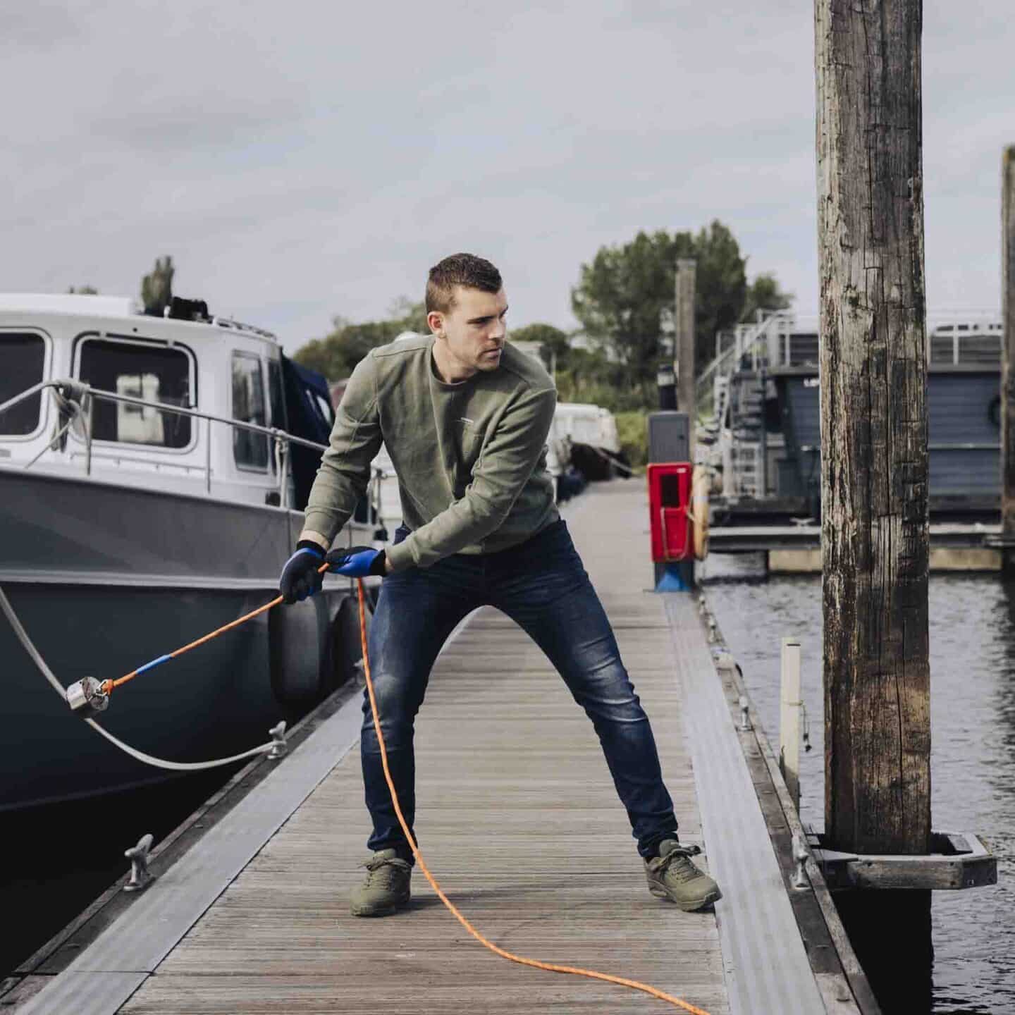 Een man die aan het magneetvissen is in de haven met een 360 magneet en oranje touw